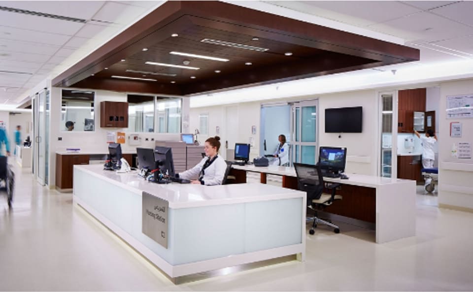 Bright, contemporary retail interior with a clean white millwork service counter and display island, a dark walnut-veneer feature ceiling raft with recessed downlights, full-height glazed partitions and light seamless resin flooring.