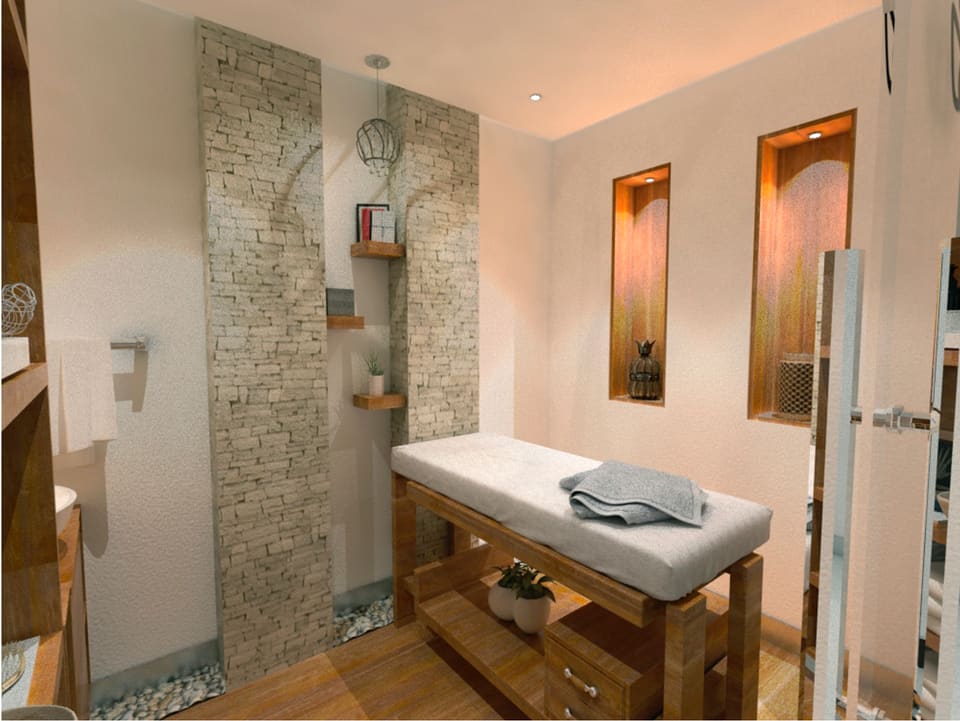 Private villa wellness room with a stacked natural-stone feature wall, timber massage bench and joinery, pebble-inset stone flooring, recessed back-lit niches and warm recessed ceiling lighting.